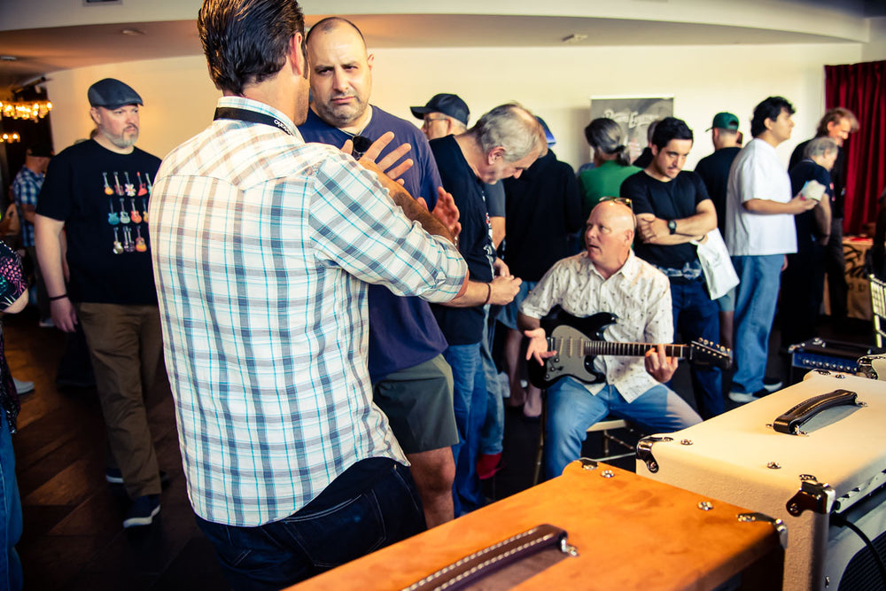A crowd around a player trying a guitar through an amp on the floor at Lago