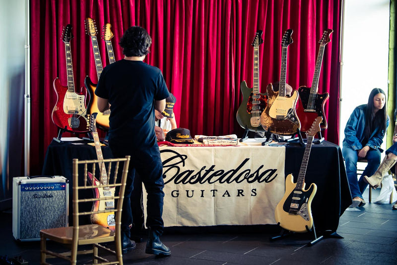 The Castedosa booth at the Beyond the Burst Guitar Showcase, guitars on stands in front of a red curtain