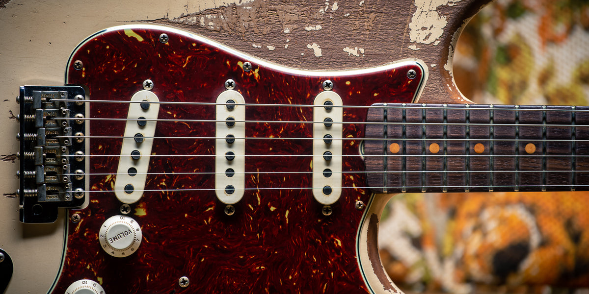 Close-up of a Fender Custom Shop '64 Stratocaster in super heavy relic Olympic White, the finish worn through to bare wood around a tortoiseshell pickguard and rosewood fingerboard
