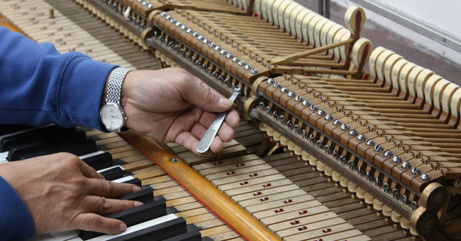 A piano technician regulating the action of an upright piano, one hand on the keys and a tool in the other
