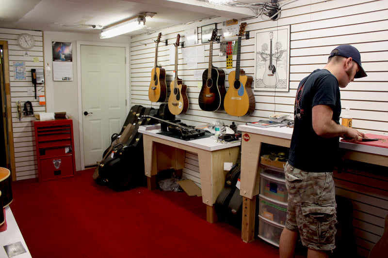 The guitar repair room at Lauzon Music, instruments waiting on the wall above the workbench